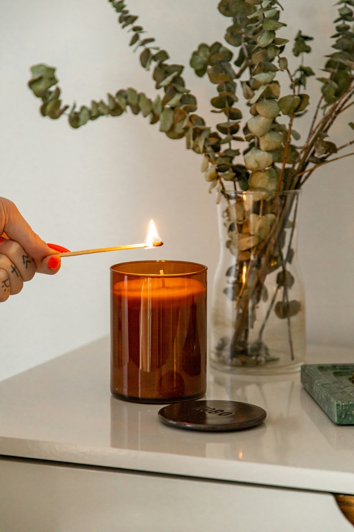 A lit candle beside a vase of eucalyptus stems
