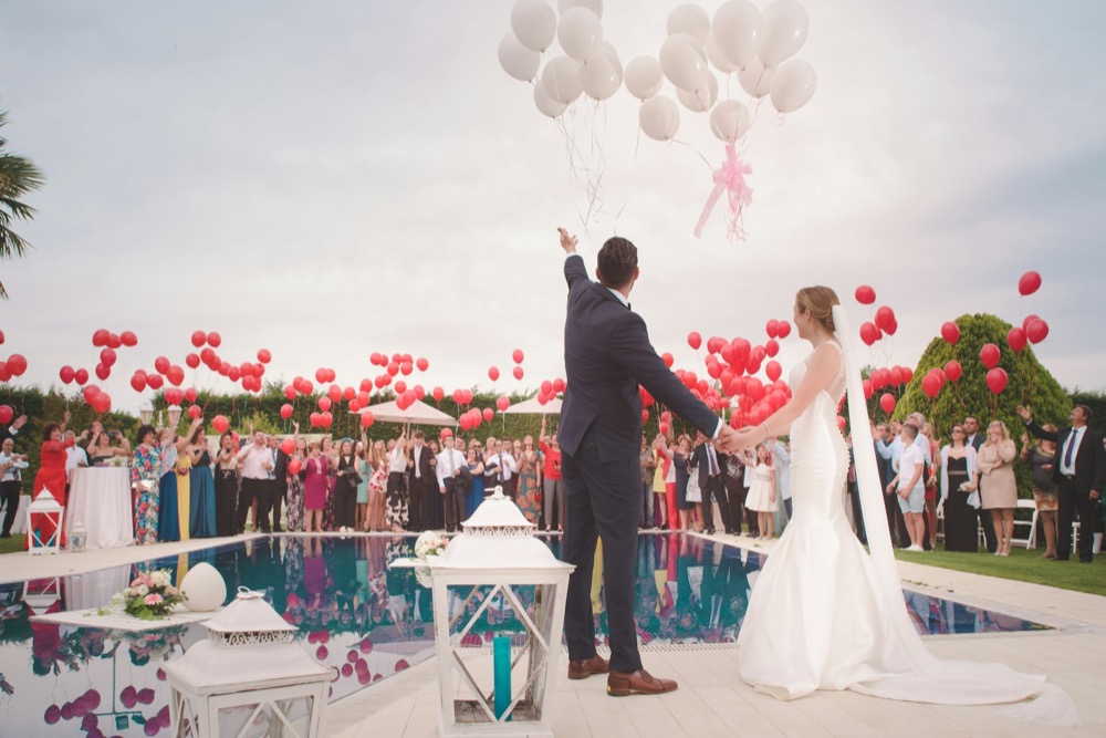 A couple celebrating beside a pool with guests and balloons