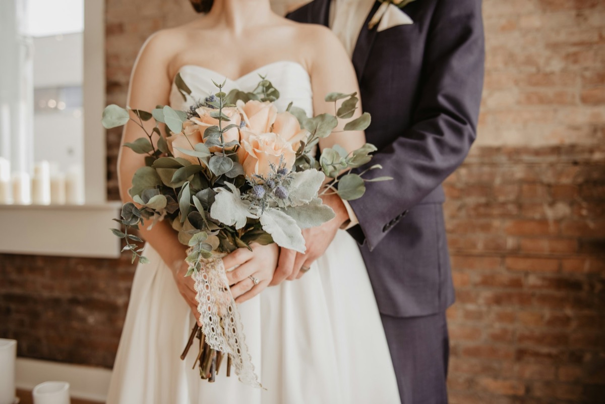 A bride holding a bouquet of blush roses and eucalyptus beside the groom