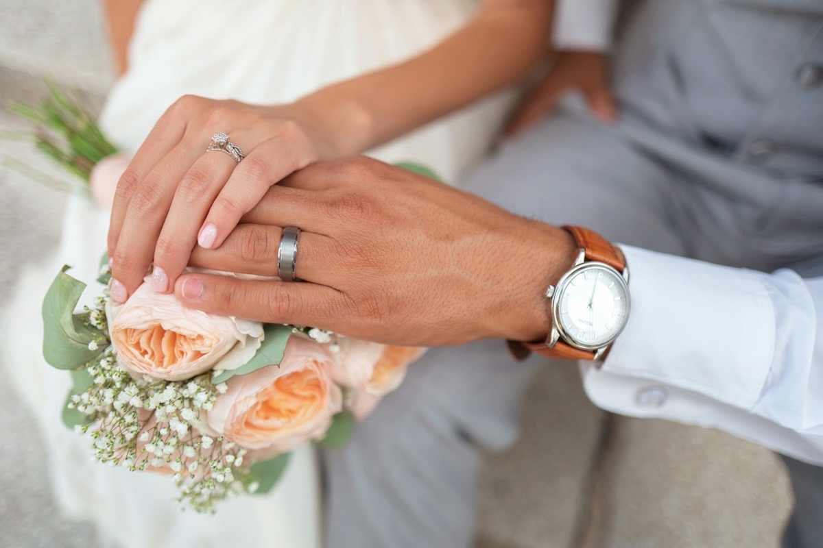 A couple holding hands over a peach and white bridal bouquet